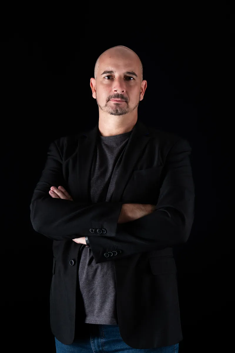 Clóvis Eduardo de braços cruzados, de blazer escuro, em fundo preto